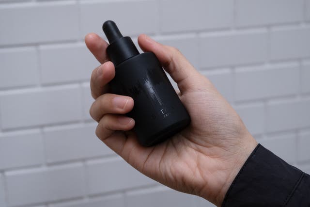 白いタイルを背景に、手に持ったBITOKUの黒い美容液ボトル