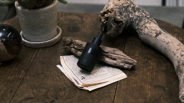 古木と英字紙の上に置いたBITOKUの黒い美容液ボトル