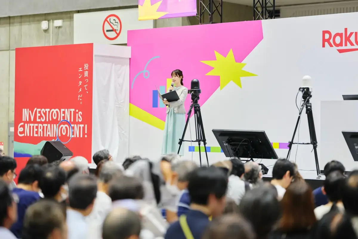 ステージ。キービジュアルを背にして話す登壇者と、見ている観客