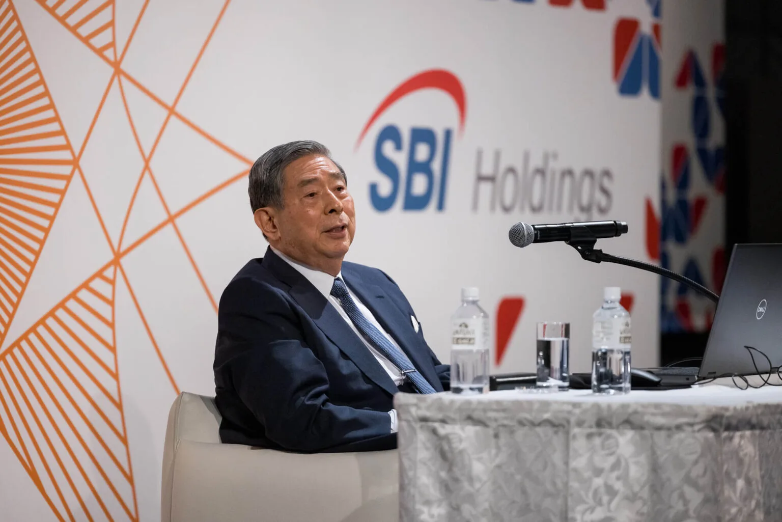 WebX Fintech EXPOのステージで話す登壇者。背面にSBI Holdingsのロゴとキービジュアル